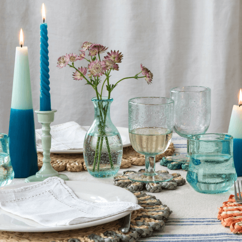 A dining table with blue candles, woven placemats and blue glassware