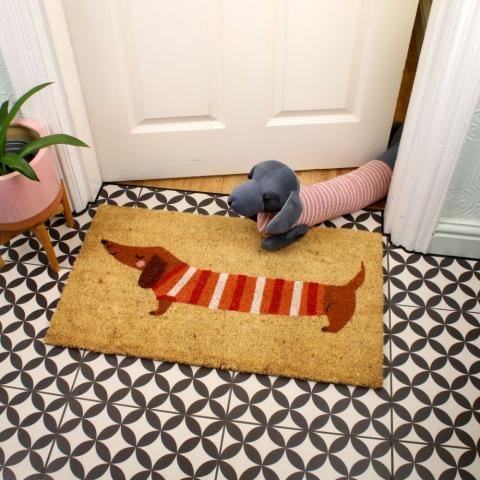 A Sausage Dog draught excluder sits on a door mat with a Sausage Dog print