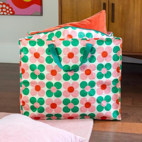 A large storage bag with a print of pink and green flowers, with an orange cushion poking out