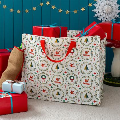 White festive shopping bag with red handles and Christmas-themed illustrations, placed among wrapped gifts.