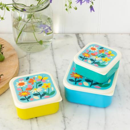 Three plastic snack boxes in yellow light blue turquoise and cream featuring prints of butterflies amongst flowers