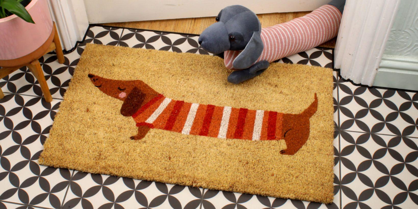 A Sausage Dog draught excluder sits on a door mat with a Sausage Dog print