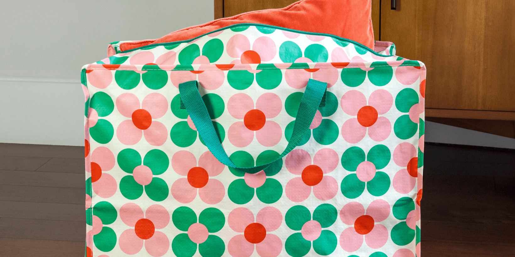 A large storage bag with a print of pink and green flowers, with an orange cushion poking out