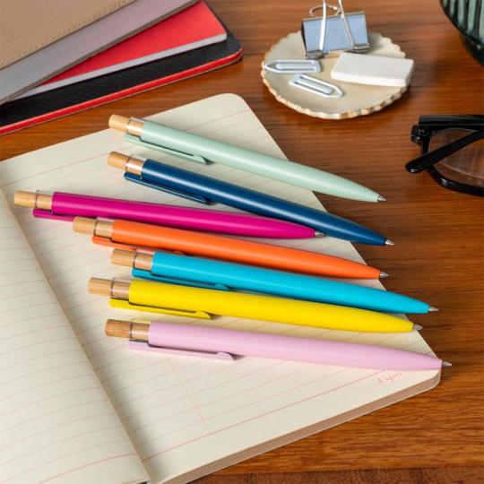 Seven colourful pens lie on an open notebook