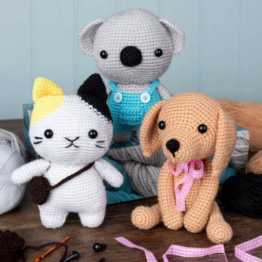 Three crocheted animals - a cat, a koala and a puppy - sit on a dark wood table